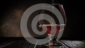 Cognac is poured into a glass. On dark background.