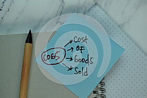 COGS - Cost Of Goods Sold write on sticky note isolated on Wooden Table