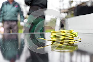 A coil of electric cable on a solar panel with technicians in the background