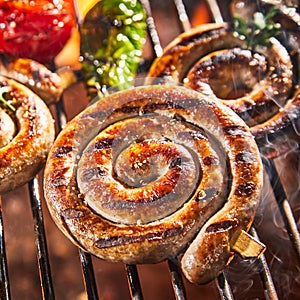 Coil of spicy beef sausage grilling on a BBQ