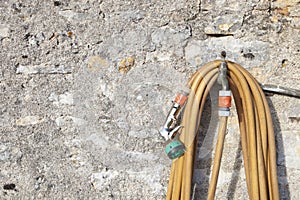 Coiled garden hose hanging on faucet against stone wall