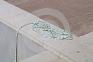 Coiled mooring line tied around cleat on a wooden dock.