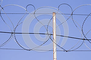 Coiled razor wire with its sharp steel barbs on top of a wire mesh perimeter fence ensuring safety and security preventing access