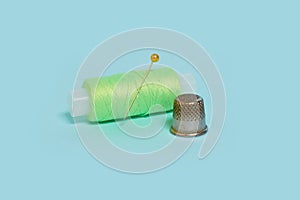 Coils with green threads, a pin and a thimble on a blue background