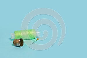 Coils with green threads, a pin and a thimble on a blue background