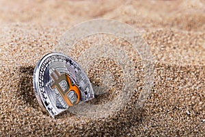 Coin bitcoin buried in the sand.