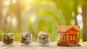 Coin in clear jar and piggy bank (Home Model) on green nature blur background. Money savings for home concept