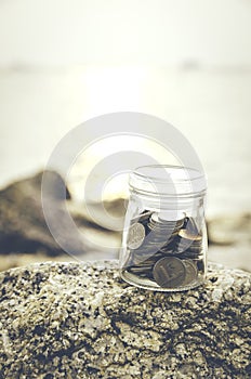 Coin in glass jar on the rock.