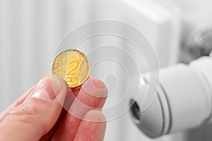 Coin in hand with a heating radiator thermostat