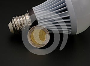 A coin leaning against a light bulb ,on a black background. Concept of blackout and expensive bill