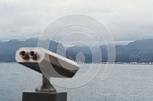 Coin operated binocular on the viewing platform in Antalya with blurred city and coast background.