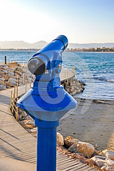 Coin operated telescope overlooking beach of maritime city.