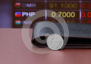 The coin of Philippine peso money and black leather wallet on brown floor with digital board of currency exchange money background