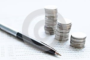 Coin stacks, pen and savings account passbook or financial statement on office desk table