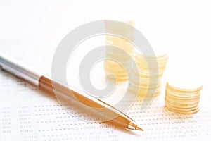 Coin stacks, pen and savings account passbook or financial statement on office desk table