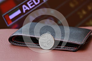 The coin of United Arab Emirates one dirham money on reverse and black leather wallet on brown floor with digital board of