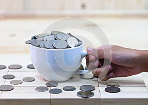 The coin in a white coffee cup rests on a wooden table and aroun