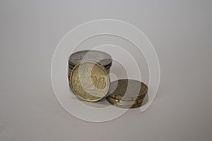A coin worth twenty euro cents stands upright next to the other coins lying one on one on a white background