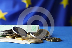 Coins and banknotes on blue table against European Union flag, closeup. Space for text