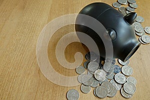 Coins and black piggy bank on wood table