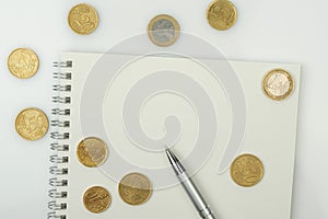 Coins, blank notepad and pen on a white background