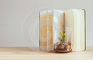 Coins in a bottle and the green tree with book background on the table, Financial planning for future expenditures.