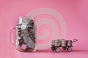 Coins in classic glass jar and coins in cart on pink background saving and investment concept