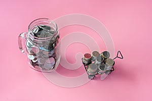 Coins in classic glass jar and coins in cart on pink background saving and investment concept