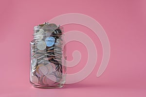 Coins in classic glass jar on pink background saving and investment concept