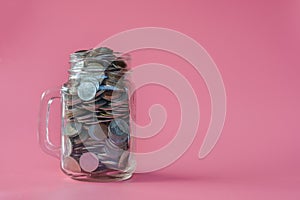 Coins in classic glass jar on pink background saving and investment concept