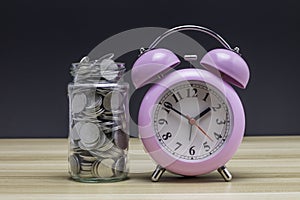 Coins in a clear glass jar with vintage clock nearby. Saving is money saved for education