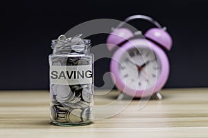 Coins in a clear glass jar with vintage clock nearby. Saving is money saved for education, paying taxes, insurance, health, travel