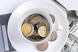 Coins from different countries placed in a cup of coffee on the wooden table. The concept of the current currency that is used in