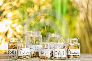 Coins for different needs in glass jars on table outdoors. Money savings concept