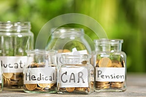 Coins for different needs in glass jars on table outdoors. Money savings concept