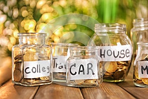 Coins for different needs in glass jars on wooden table outdoors