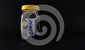 Coins in a glass jar with Loan word labelled on black background with copy space