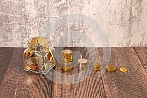 Coins in a glass jar with the small tree on top and coin ladder on table. Glass jar money saving