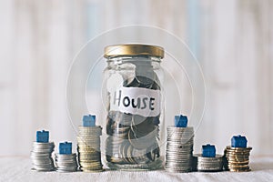 Coins and glass jar on a table with miniature house, with a note written ` HOUSE `.