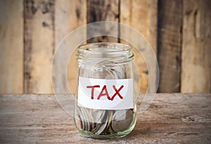 Coins in glass money jar with tax label, financial concept.