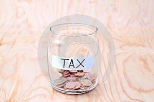 Coins in glass money jar with tax label, financial concept. Vintage wooden background
