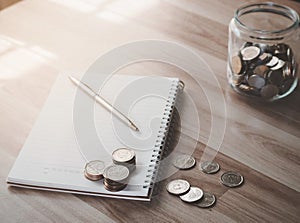 Coins money with blank white notebook on wooden table and sunlight background, finance and banking business finance concept.
