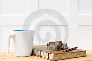 Coins, notebook and white cup on wooden table on white background