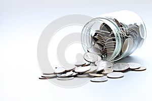 Coins scattered from glass jar on white background
