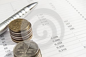 Coins and silver pen lying on financial documents, accounting and statistics concept, top view