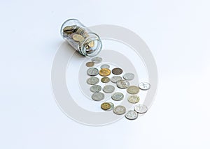 Coins spread out from a glass jar on isolated white background