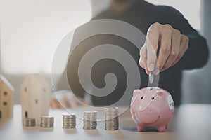 Coins stack and pink piggy with mini wood house model from model on wood table, Planning buy Real Estate, Planning to buy property