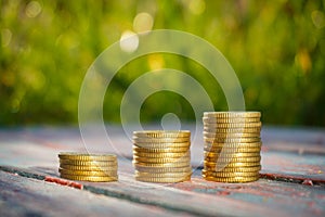 Coins stack on the wooden table with nature background.