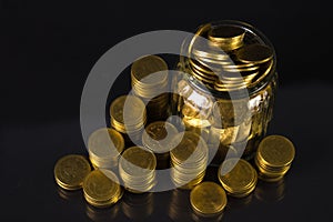 Coins stacks and gold coin money in the glass jar on dark background, for saving for the future banking finance concept.