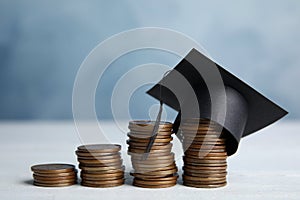 Coins and student graduation hat on wooden table against blue background. Tuition fees concept